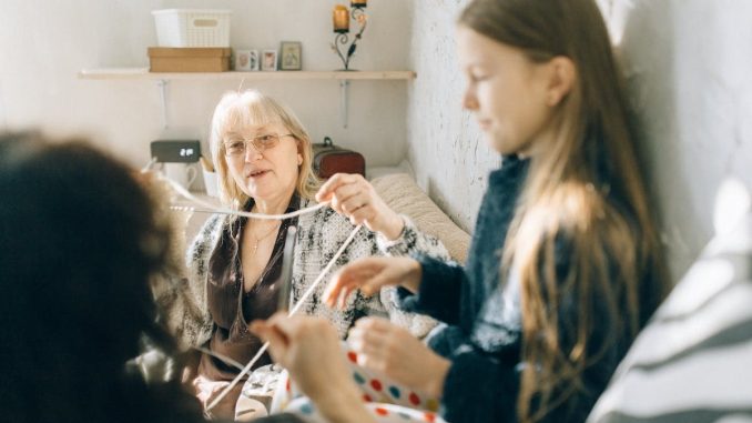 A cozy family moment with grandmother teaching granddaughter crochet indoors.